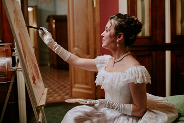 Caucasian young adult woman sitting in elegant dress painting on canvas with brush, holding palette in hand, wearing gloves and jewelry, focused on creating artwork indoors