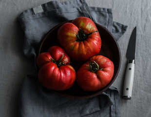 Fresh ripe large tomatoes in a ceramic bowl on a grey napkin