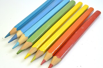 Fototapeta premium Seven brightly colored, slightly used, oversized pencils arranged in a diagonal row on a white background, showing varying degrees of sharpening and paint wear