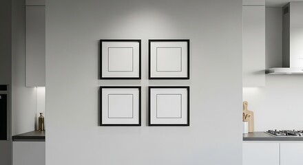 Four square frames with white mats hang on a gray wall in a modern kitchen setting, illuminated by overhead lighting.