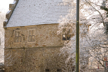 Old stone building on a cold and sunny winter day with frost covered branches in front, North...