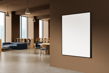 Blank poster mockup hanging on brown wall in modern office interior with wooden furniture and large...