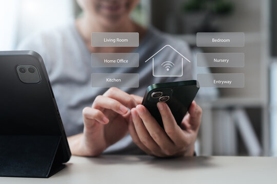 Close-up of a person using a smartphone to select Living Room, Bedroom, Kitchen, and Home Office in a smart home app; icons signal IoT connectivity, remote control, security, and energy efficiency