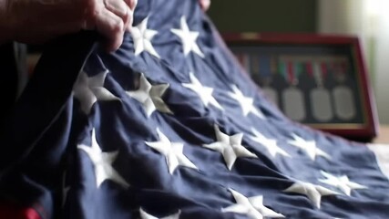 Elderly veteran folding American flag with medals in background, photorealistic motion