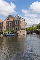 Fototapeta premium A beautiful canal view in Leiden, Netherlands, with historic Dutch gabled houses lining the tranquil water. A charming bridge in the distance adds to the idyllic European scenery.