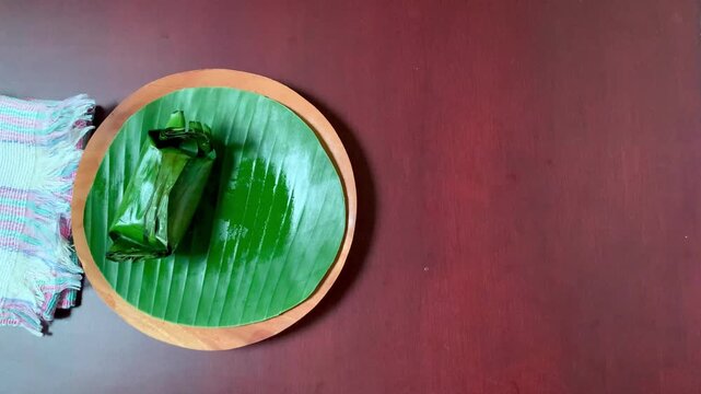 4K top view hand lifts lemper wrapped in green banana leaf. Sticky rice releases smoky aroma with tender chicken filling. Great for culinary, heritage, and festive designs.