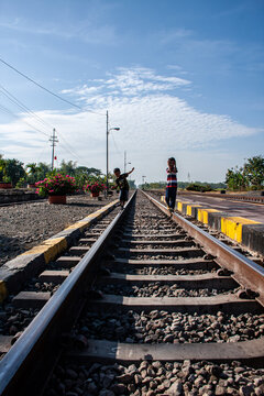 Two children are playing beside the train tracks at a quiet train station.