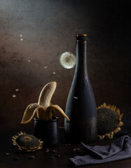 Contemporary still life with banana, dandelion in a bottle and sunflowers on a dark background