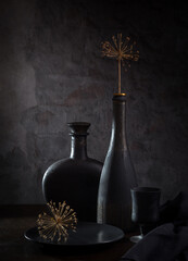 Contemporary still life with a dry branch in a black bottle and black dishes on a dark background