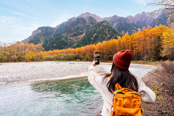 Young female tourist enjoying and taking a photo with beautiful autumn at kamikochi in Japan