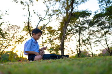 Fototapeta premium Little school boy read book on grass in city park sunset light