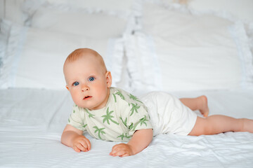 baby boy on a white bed lying on his stomach on a white bed at home, baby with blue eyes