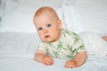 baby boy on a white bed lying on his stomach on a white bed at home, baby with blue eyes