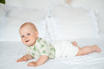 baby boy on a white bed lying on his stomach on a white bed at home, baby with blue eyes