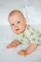 baby boy on a white bed lying on his stomach on a white bed at home, baby with blue eyes