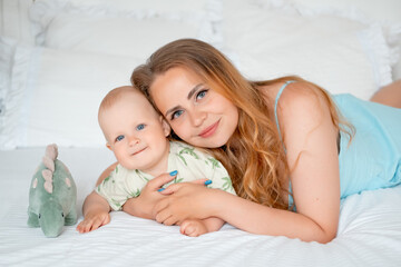 mom with a small child, mom with a newborn baby at home on the bed smiling, hugging and kissing, a...