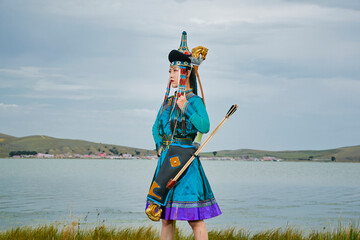 Mongolian girls dressed in traditional Mongolian attire and holding bows and arrows by a lake on...