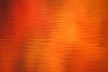 Abstract autumn background with reflections of red orange and golden leaves on calm water ripples