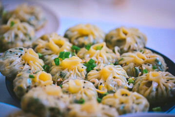 A plate of steamed dumplings garnished with chopped green onions and sesame seeds, ready to be...