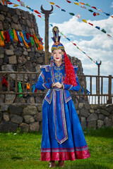 Naklejka premium Mongolian girls dressed in luxurious Mongolian costumes in front of an obo on the grassland