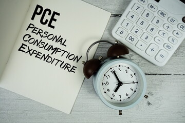 PCE Personal Consumption Expenditure text on paper notebook page with alarm clock and calculator on...