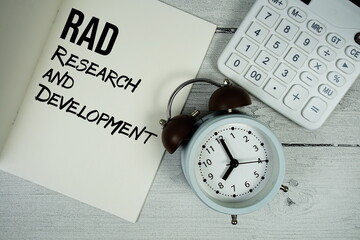Research and Development text on paper notebook page with alarm clock and calculator on wooden...