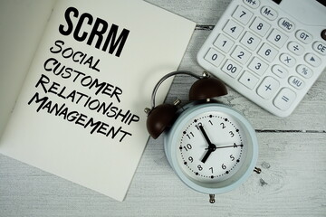 SCRM Social Customer Relationship Management text on paper notebook page with alarm clock and...