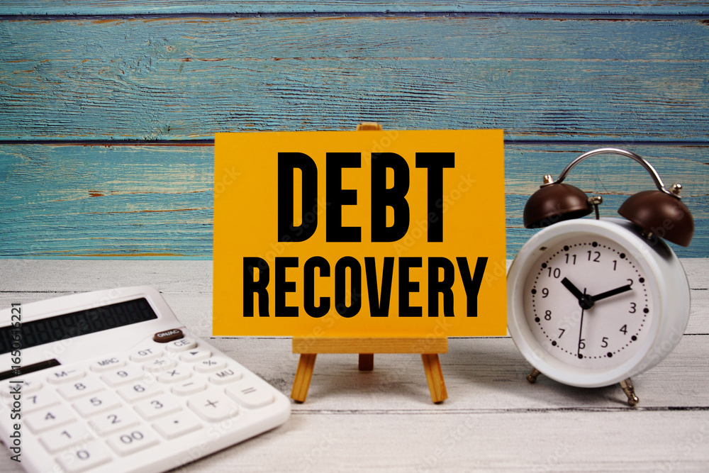 Poster debt recovery text written on paper card with calculator and alarm clock on wooden background