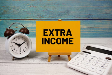 Extra Income text written on paper card with calculator and alarm clock on wooden background