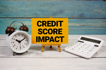 Credit Score Impact text written on paper card with calculator and alarm clock on wooden background