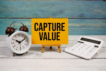 Capture Value text written on paper card with calculator and alarm clock on wooden background