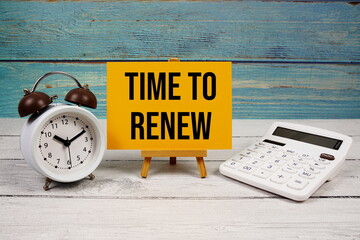 Time To Renew text written on paper card with calculator and alarm clock on wooden background
