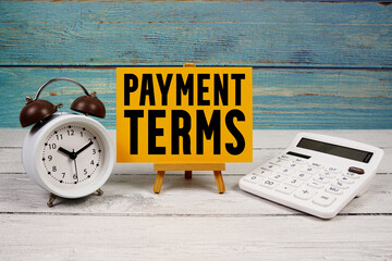 Payment Terms text written on paper card with calculator and alarm clock on wooden background