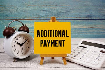 Additional Payment text written on paper card with calculator and alarm clock on wooden background