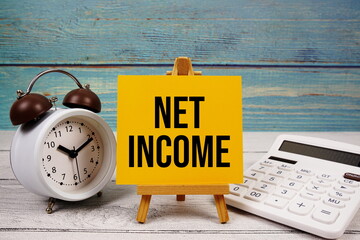 Net Income text written on paper card with calculator and alarm clock on wooden background