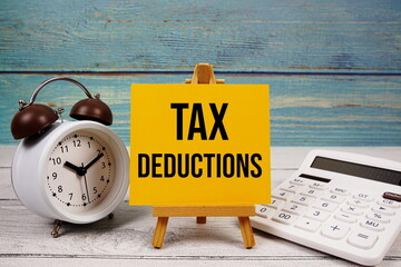 Tax Deductions text written on paper card with calculator and alarm clock on wooden background