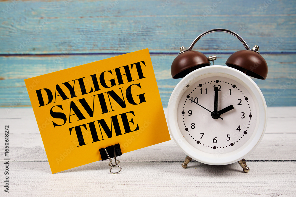 Poster daylight saving time text written on paper card with alarm clock on wooden background