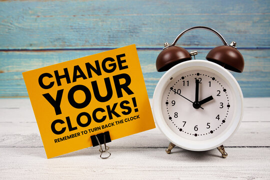 Change Your Clocks  text written on paper card with alarm clock on wooden background