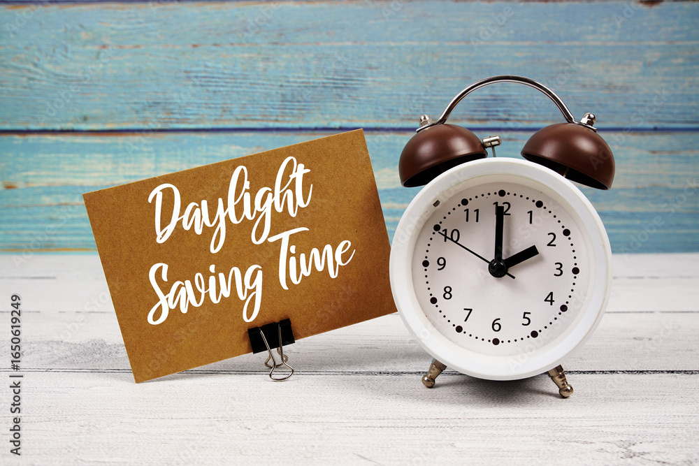Poster daylight saving time text written on paper card with alarm clock on wooden background