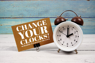 Change Your Clocks  text written on paper card with alarm clock on wooden background
