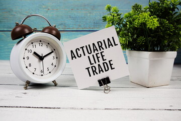 Actuarial Life Trade text written on paper card with alarm clock on wooden background
