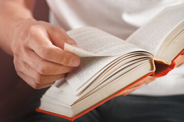 man's hand turns the page of a red hardcover book