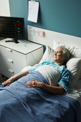 Senior Caucasian woman lying in hospital bed with oxygen tube, resting with eyes closed, connected...