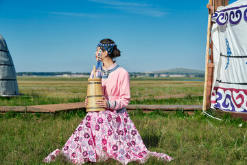 Fototapeta premium A Mongolian girl wearing Mongolian attire and holding a bucket of milk tea in front of a yurt.