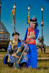 A young couple in traditional Mongolian clothing in front of a yurt on the grassland