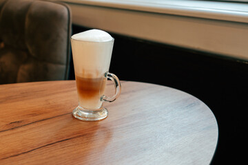 Delicious layered coffee served in a clear glass on a wooden table in a cozy cafe atmosphere
