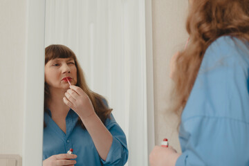 Beautiful elderly woman with long hair doing skin care in front of mirror in stylish elegant beige...