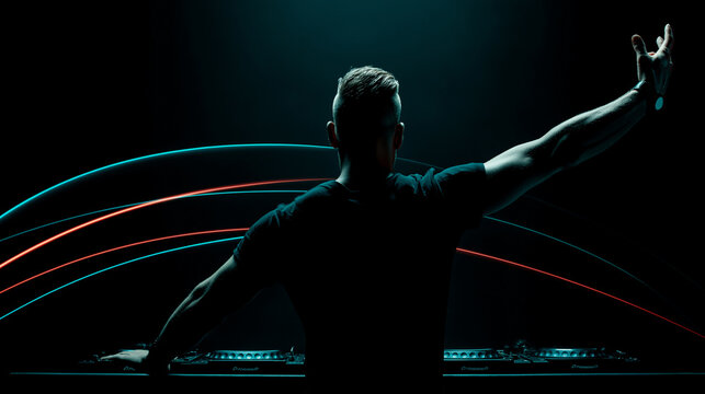 Silhouette of male DJ in black t-shirt facing crowd, arm raised, colorful arcs of cyan and red lights above booth, dark concert setting