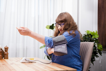 Beautiful elderly woman removes tonometer cuff from arm after measuring blood pressure in stylish...