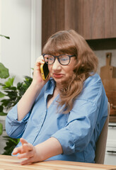 Beautiful elderly woman in glasses talking emotionally on smartphone in yellow case in stylish...